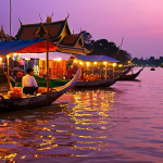 **Prompt 1: Enchanting Riverside Twilight in Phnom Penh:** A vibrant, atmospheric wide shot of Phnom Penh's Riverside (Tonle Sap River) at twilight. The sky glows with incredible hues of orange, pink, and purple as the sun sets or rises. Traditional wooden boats gently drift on the calm river. Along the bustling promenade, modern cafes with inviting lights and lively riverside restaurants are visible. Street vendors are preparing fresh Khmer coffee. In the background, hints of the majestic Royal Palace or Silver Pagoda are illuminated. The scene captures a unique blend of historical charm and pulsating nightlife, with a sense of calm and wonder.